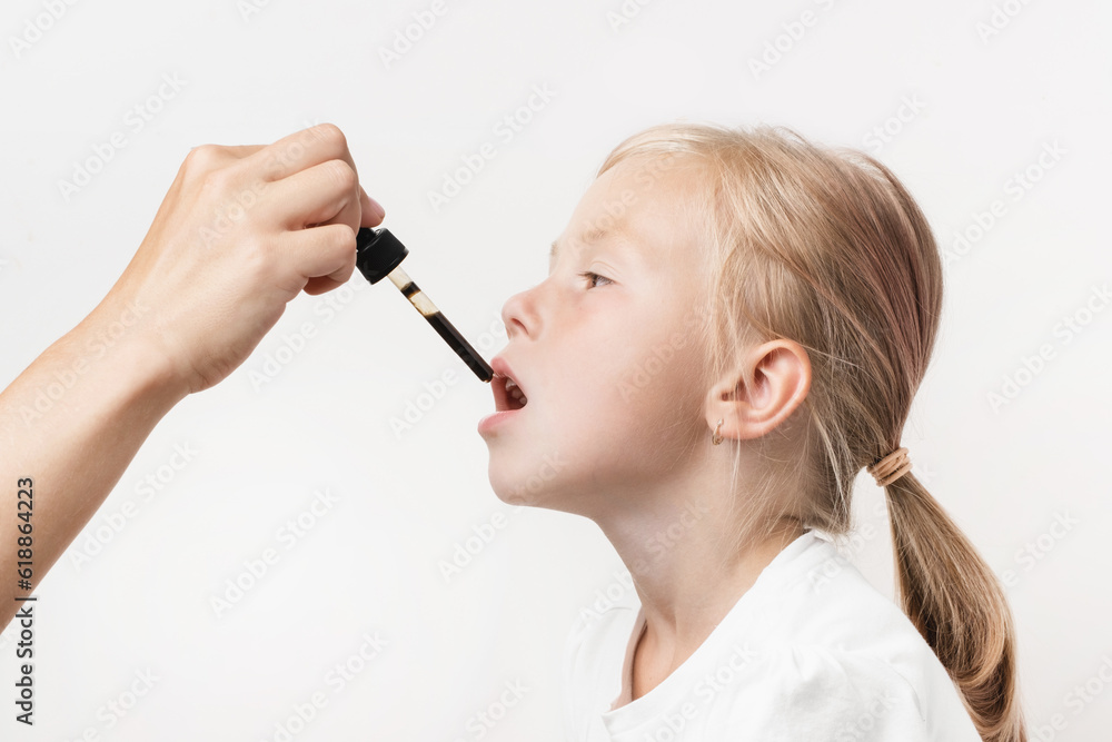 Portrait of happy cute caucasian girl taking supplement or medicine syrup in pipette on white background. Fever reducing treatment for children. Mild sedative for little kids. High temperature cure