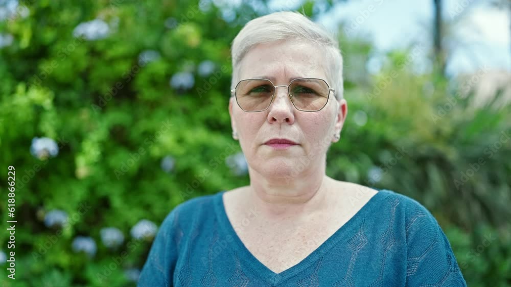 Middle age grey-haired woman standing with serious expression at park Middle age grey-haired woman standing with serious expression at park