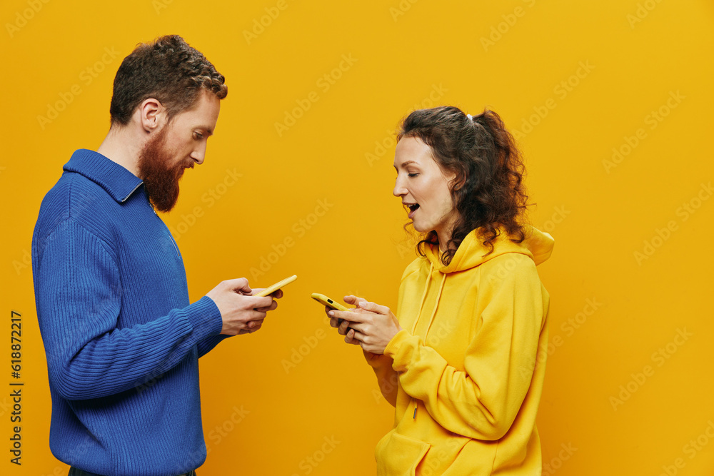 Woman man cheerful couple with phones in hand social networking and communication crooked smile fun and fight, in yellow background. The concept of real family relationships, freelancers, work online. Woman man cheerful couple with phones in hand social networking and communication crooked smile fun and fight, in yellow background. The concept of real family relationships, freelancers, work online.