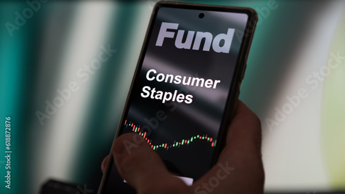 An investor's analyzing the consumer staples etf fund on a screen. A phone shows the prices of consumer staples equities. To invest in ETFs