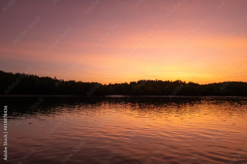 Fototapeta premium Colorful sky and the sea during the sunrise, with silhouette of the forest on the background