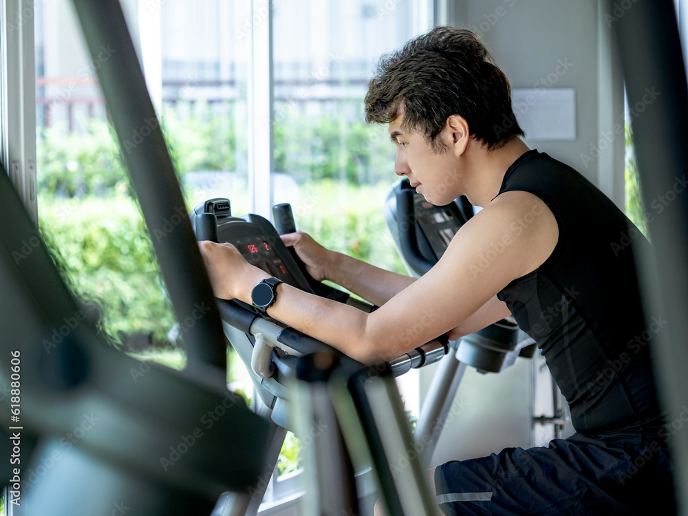 Φωτογραφία Active Asian sport man in black sportswear cycling on an upright stationary bike or upright exercise bicycle