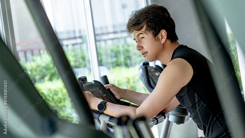Φωτογραφία Active Asian sport man in black sportswear cycling on an upright stationary bike or upright exercise bicycle