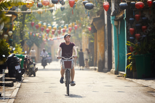 Tourist riding bicycle in old town. Street of ancient city decorated with traditional lanterns, Hoi An, Vietnam...