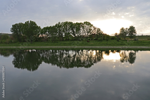 Sunset on the river. The rays of the sun and the trees are reflected in the water.