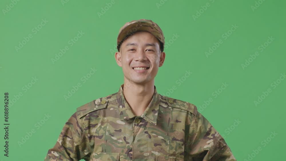 Close Up Of Asian Man Soldier Standing With Arms Akimbo Looking At Camera And Smiling In The Green Screen Background Studio
