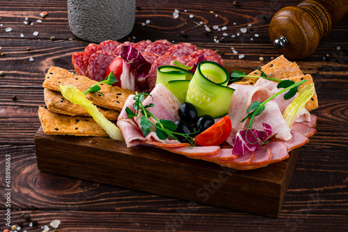 Banquet meat board with slices of sausage, ham, cucumber, cherry tomatoes, olives, lettuce and dried bread.