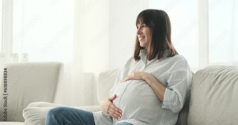 Beautiful pregnant woman finds solace on the couch. With a radiant smile illuminating her face, she delicately strokes her rounded belly, emanating a sense of love and tenderness. Beautiful pregnant woman finds solace on the couch. With a radiant smile illuminating her face, she delicately strokes her rounded belly, emanating a sense of love and tenderness.