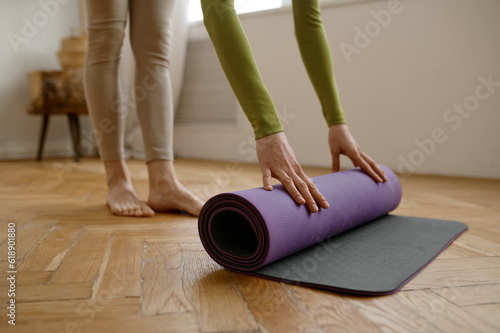 Closeup woman rolling yoga mat on wooden floor