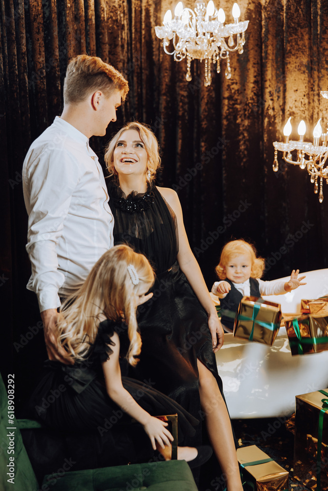 Merry Christmas and Happy Holidays! Cheerful and happy family with Christmas presents in golden wrappings and dark background. Children are having fun. Loving family with gifts in the room.
