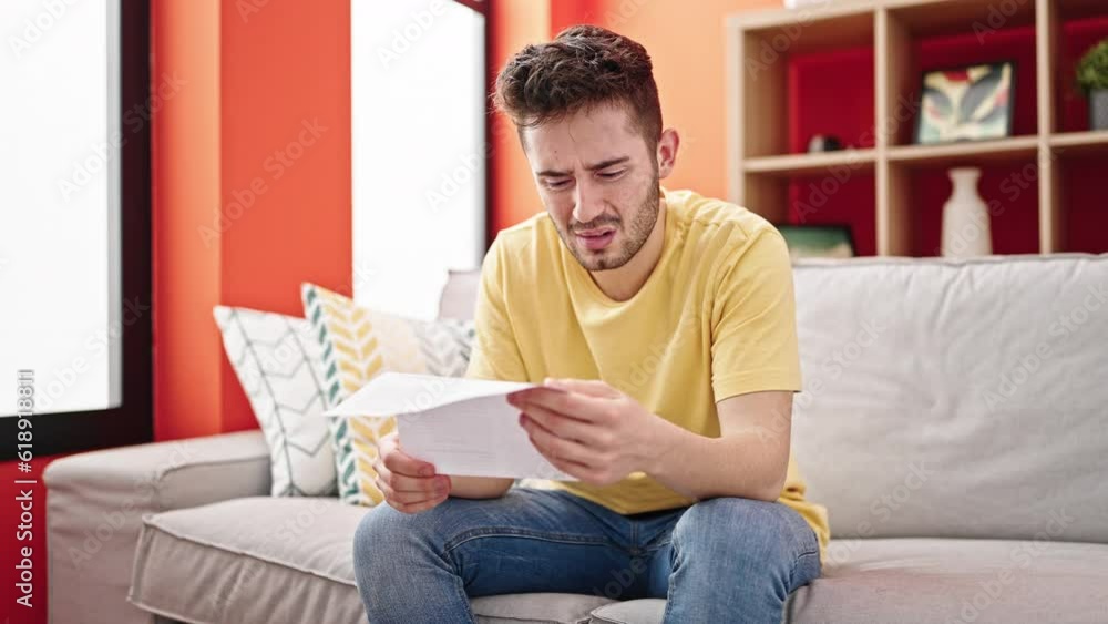 Young hispanic man reading document sitting on the sofa at home Young hispanic man reading document sitting on the sofa at home
