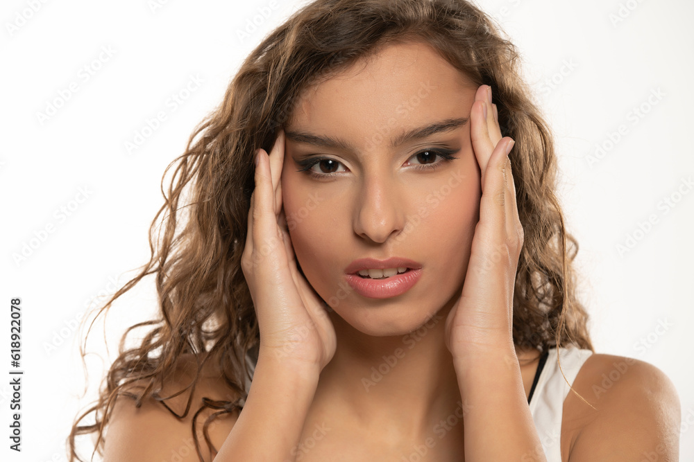 Young brunette woman tightening her face skin with her palms on a white background Young brunette woman tightening her face skin with her palms on a white background