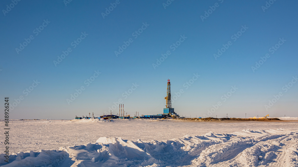 A gas field in the Arctic. Polar winter day. In the foreground is a snowy tundra. In the background is a drilling rig and industrial infrastructure