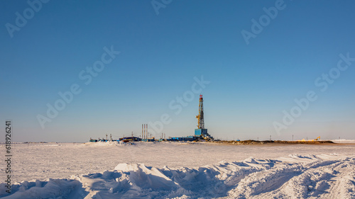 A gas field in the Arctic. Polar winter day. In the foreground is a snowy tundra. In the background is a drilling rig and industrial infrastructure