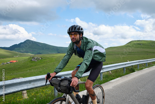 Man cyclist riding a gravel bike with a view of the mountains.Practicing cycling on open country road.Empty mountain road.Cycling adventure in Romania. Bucegi Mountains. photo