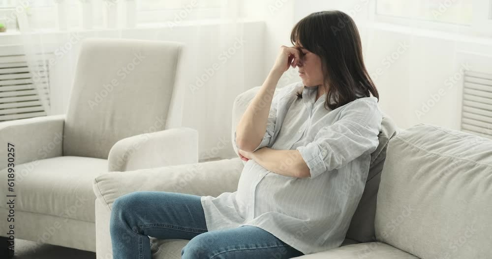 In a cozy living room, a pregnant woman sits on the couch, lost in thought. With a pensive expression, she gently caresses her belly, contemplating the journey of motherhood. In a cozy living room, a pregnant woman sits on the couch, lost in thought. With a pensive expression, she gently caresses her belly, contemplating the journey of motherhood.