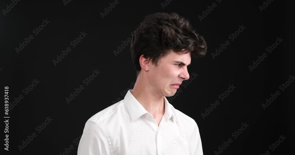 A concerned Caucasian man as he reacts with profound disgust against a striking black background. With furrowed brows and a look of disdain, he expresses his strong aversion to a situation or object. A concerned Caucasian man as he reacts with profound disgust against a striking black background. With furrowed brows and a look of disdain, he expresses his strong aversion to a situation or object.