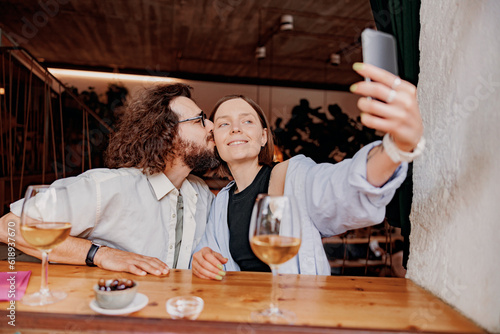 Man kissing woman in a cheek and take a selfie while they drinking wine in bar during romantic date