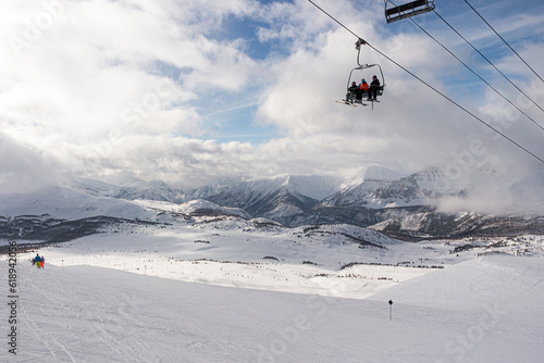 Mounain range covered in snow and clouds over them with gondola car and skiers © Martin