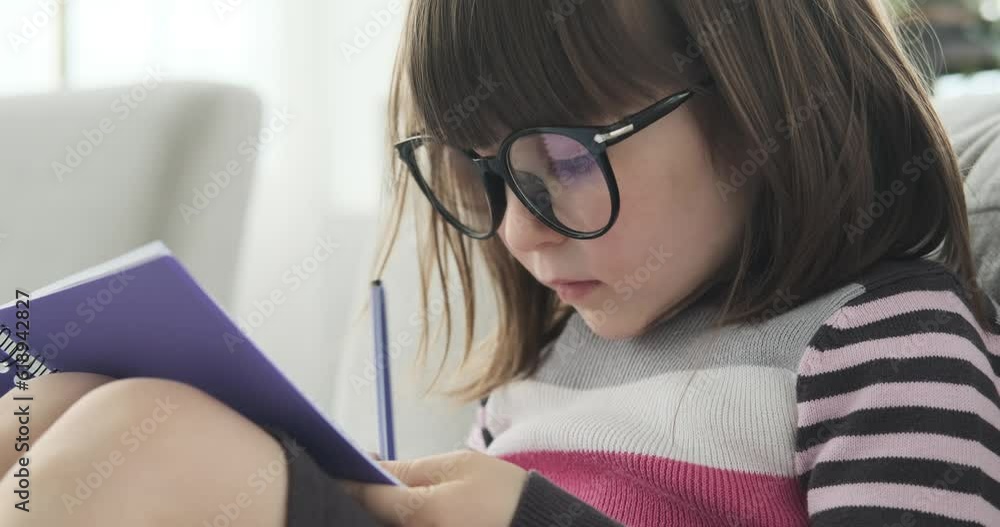 Thoughtful girl of Caucasian descent, seated on the lounge couch. With her glasses perched upon her nose, she dedicates her attention to writing in a notebook, Thoughtful girl of Caucasian descent, seated on the lounge couch. With her glasses perched upon her nose, she dedicates her attention to writing in a notebook,