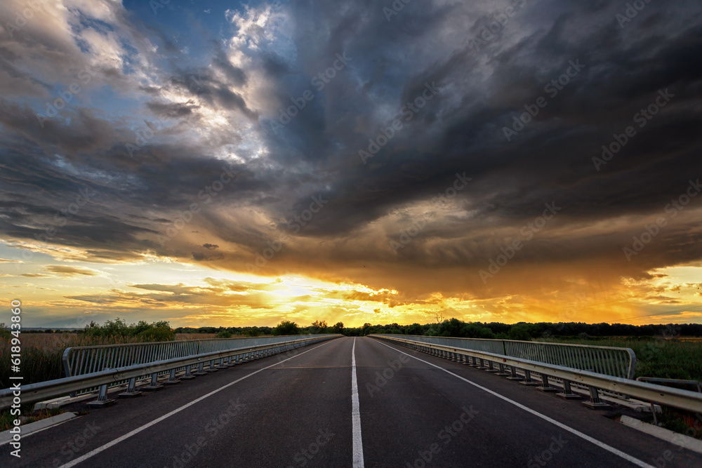 Empty asphalt highway outside the city, sunset with storm clouds
