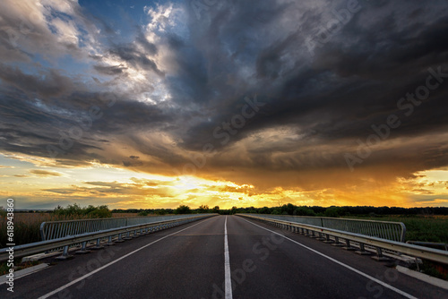Empty asphalt highway outside the city, sunset with storm clouds © pobaralia