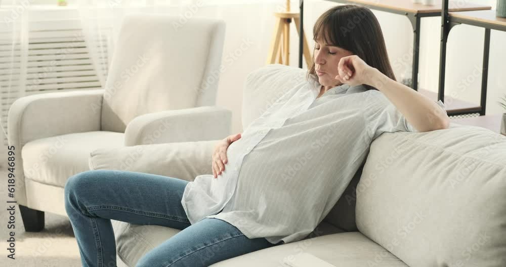 A tired pregnant woman finds solace on a comfortable couch. With a serene expression and a gentle touch, she lovingly caresses her baby bump, bestowing her wearied body with tenderness and care. A tired pregnant woman finds solace on a comfortable couch. With a serene expression and a gentle touch, she lovingly caresses her baby bump, bestowing her wearied body with tenderness and care.