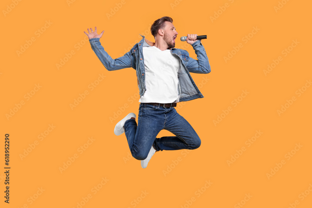 Handsome man with microphone singing and jumping on yellow background Handsome man with microphone singing and jumping on yellow background