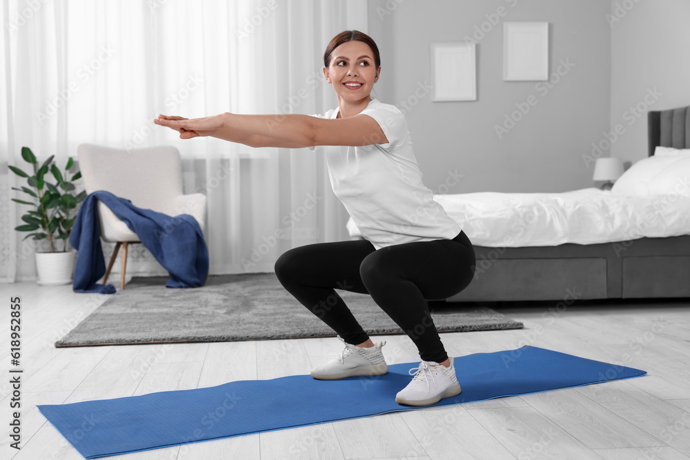 Fototapeta premium Morning exercise. Happy woman squatting at home