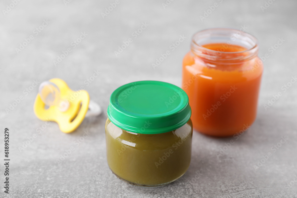 Jars with healthy baby food and pacifier on light grey table Jars with healthy baby food and pacifier on light grey table