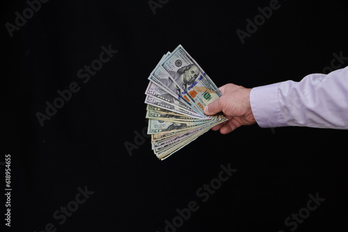 Male hand offering money, American dollar bills, USA currency against black background, exchange, trade and winning money concept, finance and business