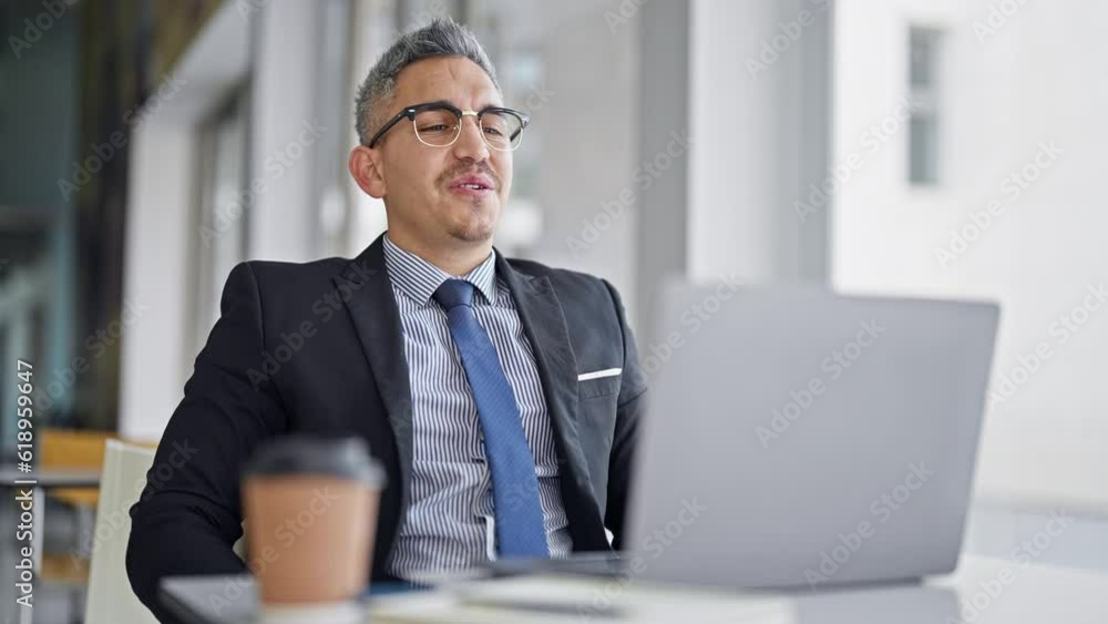 Young hispanic man business worker using laptop taking glasses off at office Young hispanic man business worker using laptop taking glasses off at office