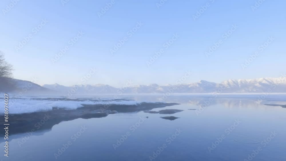 Hot spring steam drifting over icy shore and calm water of caldera lake at dawn in winter Hot spring steam drifting over icy shore and calm water of caldera lake at dawn in winter