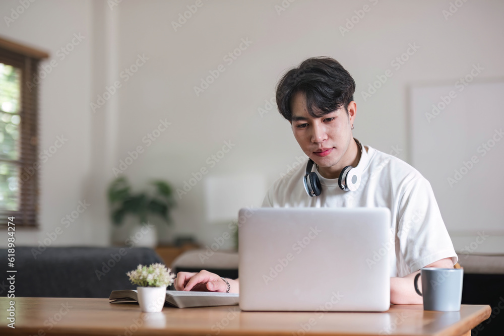 A focused young Asian male college student or freelancer using his digital tablet at a table in his living room. A focused young Asian male college student or freelancer using his digital tablet at a table in his living room.