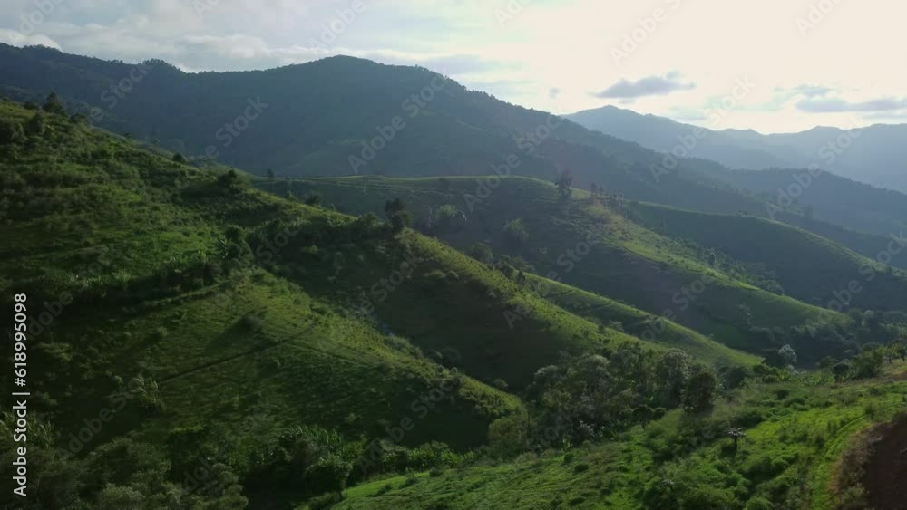 Scenic of idyllic rolling hills landscape with blooming meadows and mountain ranges in the background on a beautiful sunny day with blue sky and clouds in springtime. Scenic of idyllic rolling hills landscape with blooming meadows and mountain ranges in the background on a beautiful sunny day with blue sky and clouds in springtime.