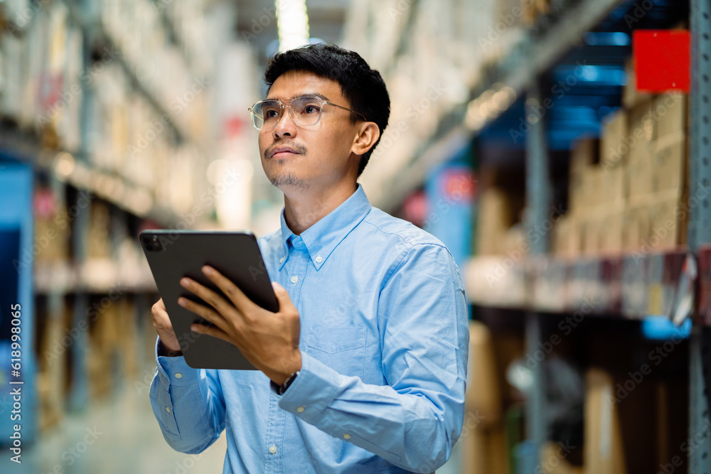 Logistics and export business Factory warehouse. business Industrial. warehouse. Asian male worker in security suit with tablet computer looking for items in a large warehouse. Logistics and export business Factory warehouse. business Industrial. warehouse. Asian male worker in security suit with tablet computer looking for items in a large warehouse.