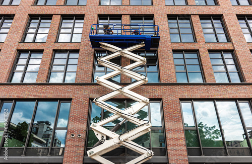 maintenance workers are repairing a modern building facade from an elevating scissor lift aerial work platform photo