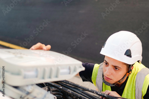 Working woman.Female engineer doing fiber optic installation from a ladder with safety helmet and high visibility vest.High speed internet and telecommunications.
