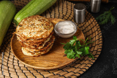 Plate of tasty zucchini fritters with sour cream on black background
