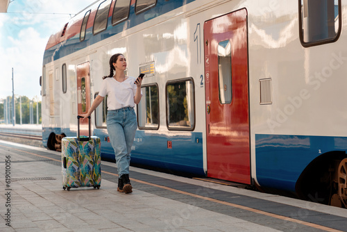 Young pretty woman walking to departure holds her luggage. Train station is in background. Concept of vacation and business trip