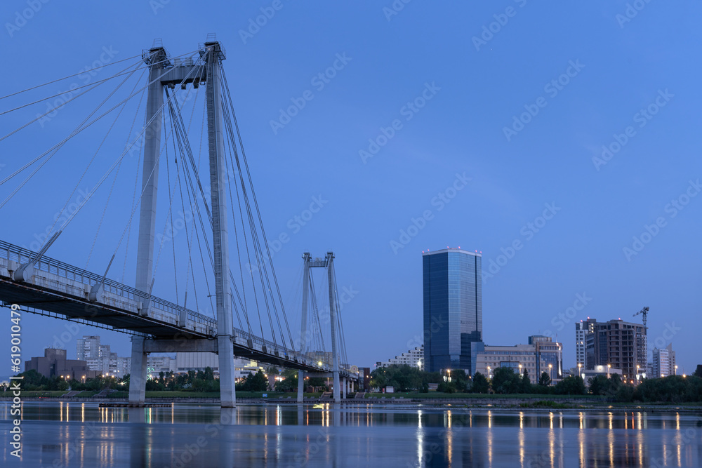 Obraz premium Panorama of the night city of Krasnoyarsk. View of the Vinogradovsky suspension bridge and the outlines of buildings in the morning, at night before dawn. lights of the Yenisei
