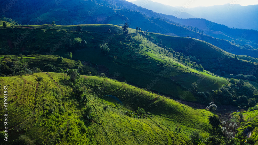 Scenic of idyllic rolling hills landscape with blooming meadows and mountain ranges in the background on a beautiful sunny day with blue sky and clouds in springtime. Scenic of idyllic rolling hills landscape with blooming meadows and mountain ranges in the background on a beautiful sunny day with blue sky and clouds in springtime.