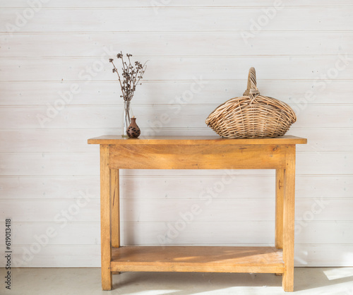 Oak side table with acccessories including seedpod, dried twigs and wicker basket against white painted timber wall (selective focus)