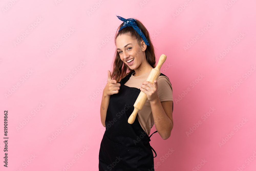 Young woman holding a rolling pin pointing to the front and smiling Young woman holding a rolling pin pointing to the front and smiling