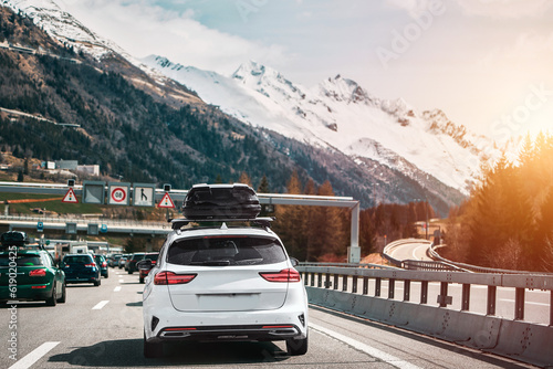 White wagon with roof box storage on the highway in Switzerland. Modern family car adventures in the Alpine Mountains in Europe. Plastic luggage compartment on a car roof. Road trip getaway concept. © AlexGo
