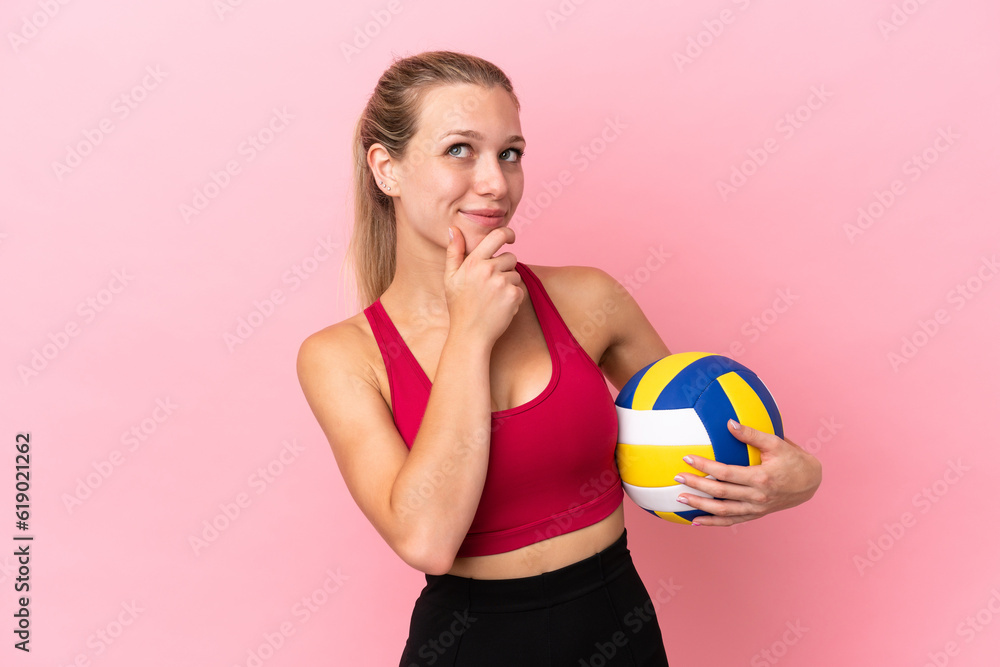 Young caucasian woman playing volleyball isolated on pink background and looking up