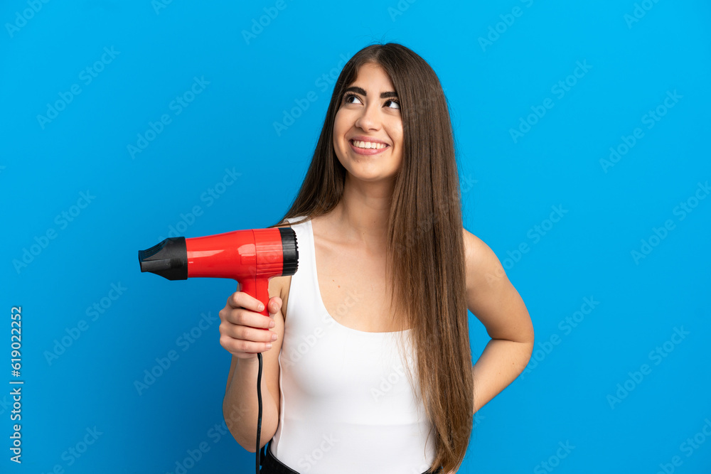 Young caucasian woman holding a hairdryer isolated on blue background thinking an idea while looking up Young caucasian woman holding a hairdryer isolated on blue background thinking an idea while looking up
