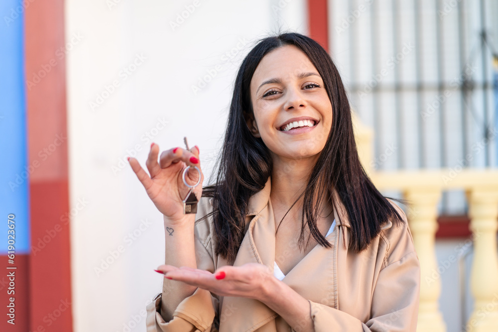 Young woman at outdoors holding home keys with happy expression Young woman at outdoors holding home keys with happy expression