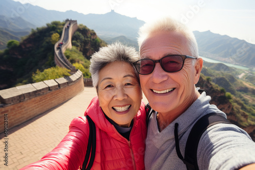 A happy elderly tourist couple take a selfie in China with the Great Wall in the background. Travel retirement concept. AI generated. © serperm73