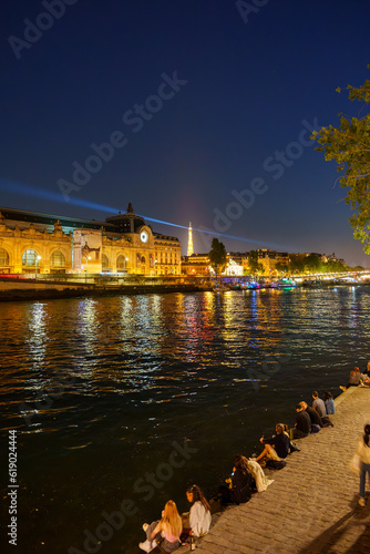 夜のセーヌ川沿いでくつろぐ人々とエッフェル塔などが輝くパリの夜景
